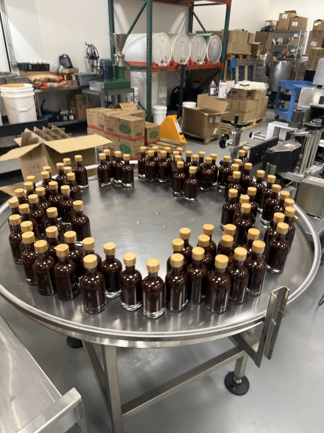 Filled sauce bottles with wood-look caps on a stainless steel bottling table
