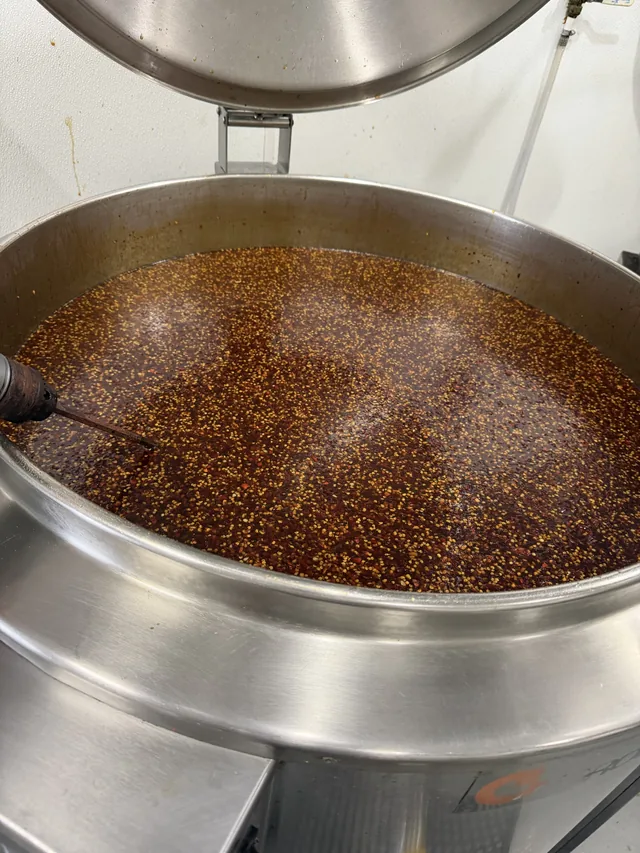 A batch of sauce with visible seasoning in a stainless steel mixing kettle